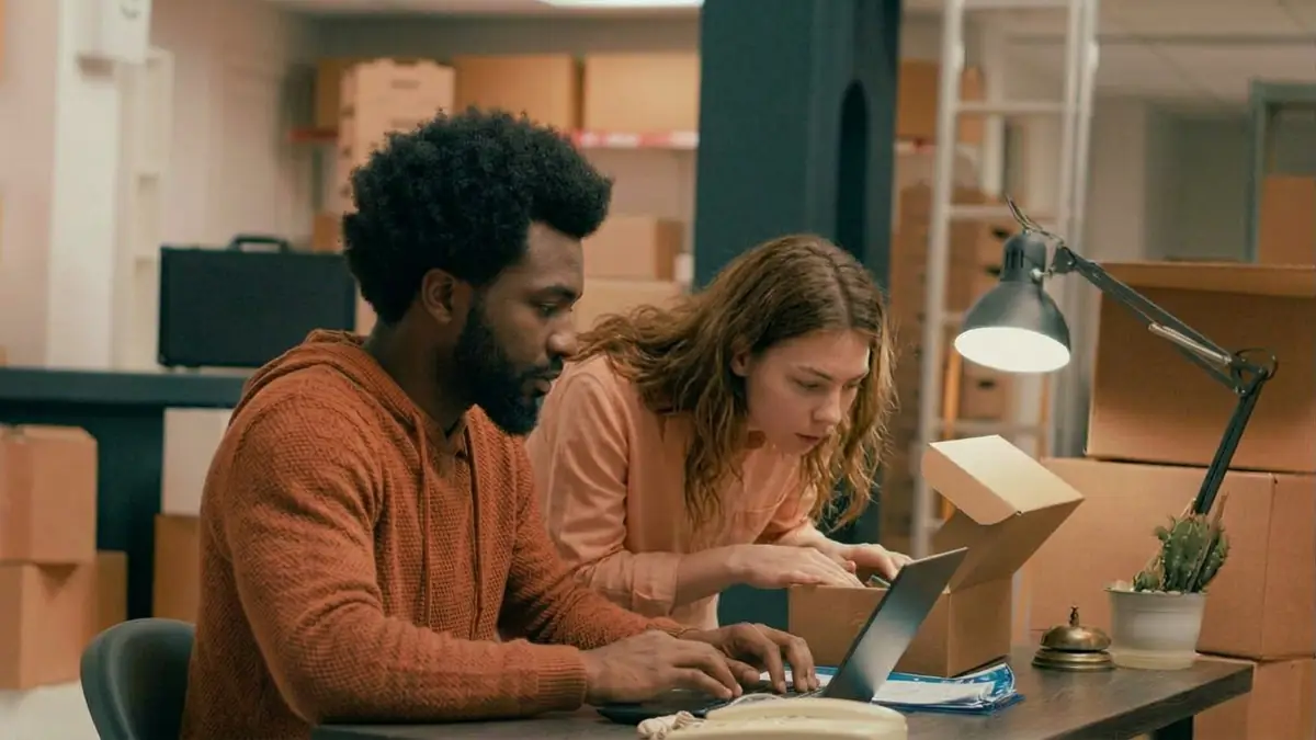 Dos personas de una tienda online revisando pedidos en el portátil entre cajas